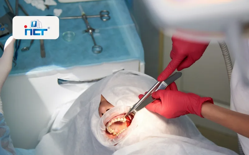 Dental procedure in progress: patient with mouth open, dentist and assistant using surgical tools under sterile drapes.