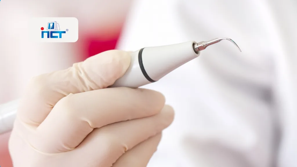 Gloved hand holding a dental scaler with a curved tip, ready for cleaning teeth (logo in background).